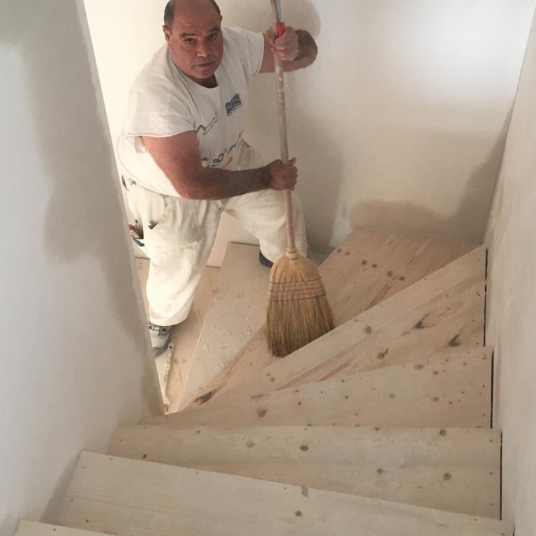 Ein Mann kehrt auf einer unbehandelten Holztreppe in einem Innenraum.